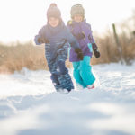 Two kids race around in the snow togehter.