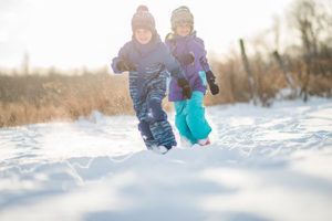 Two kids race around in the snow togehter.