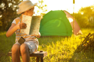 A child reads a book near a tent.