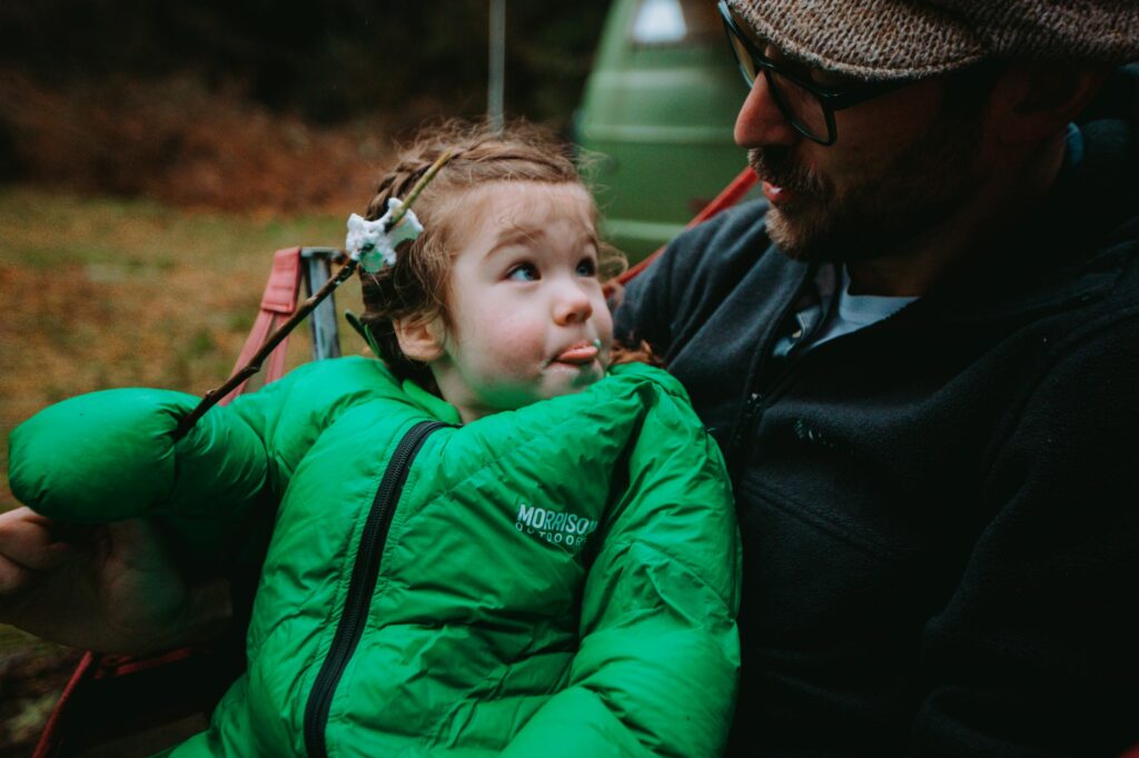 A dad holds his young child, who is wearing a Morrison Outdoors Gear sleeping bag, while hiking.