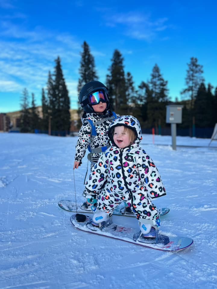 Two young kids stand on snowboards, while enjoying a winter day in Breckenridge, one of the best winter vacations for families.