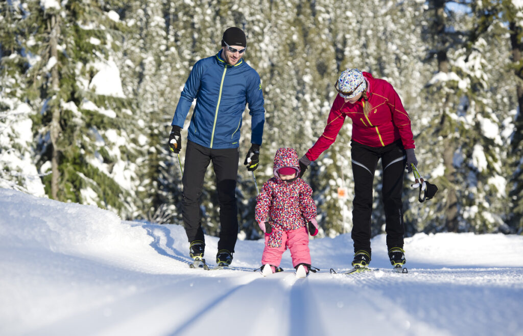 A family of three with a toddler hikes along a snowy path in Whistler, one of the best winter vacations for families.
