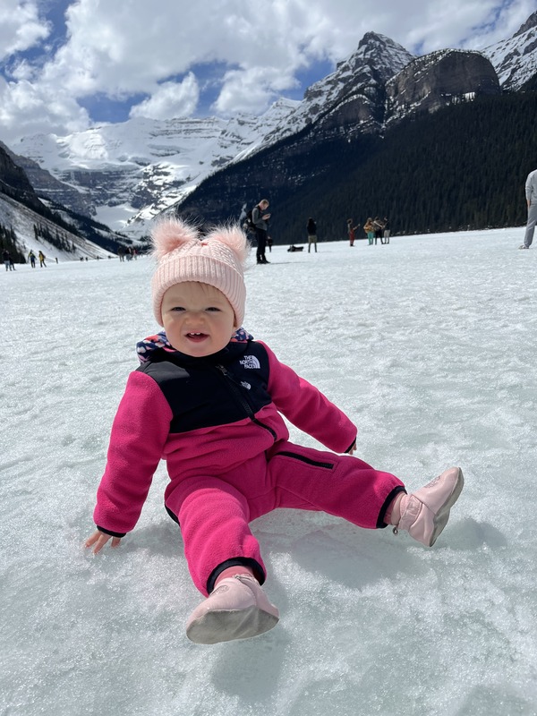 A toddler girl sits on frozen Lake Louise, one of the best winter destinations for families.
