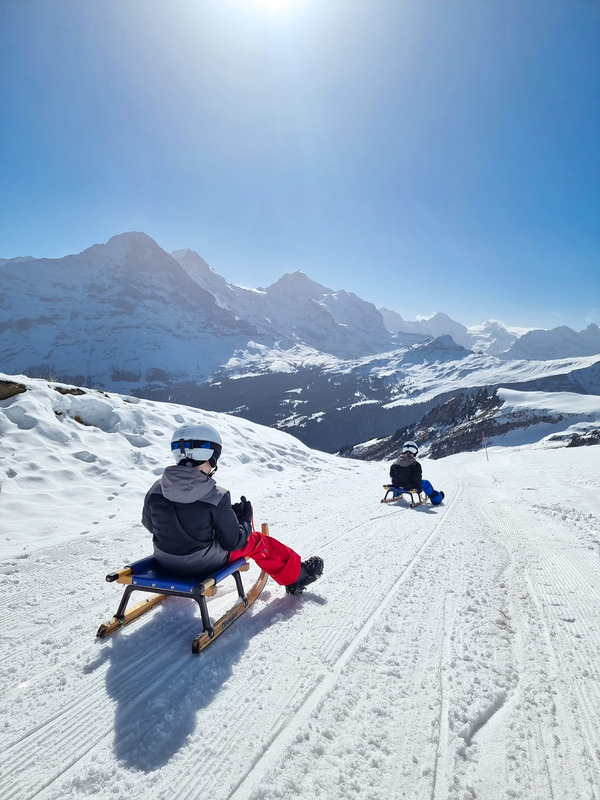 Two kids sled down a snowy hill in Switzerland, one of the best places to visit in Europe with outdoor kids.