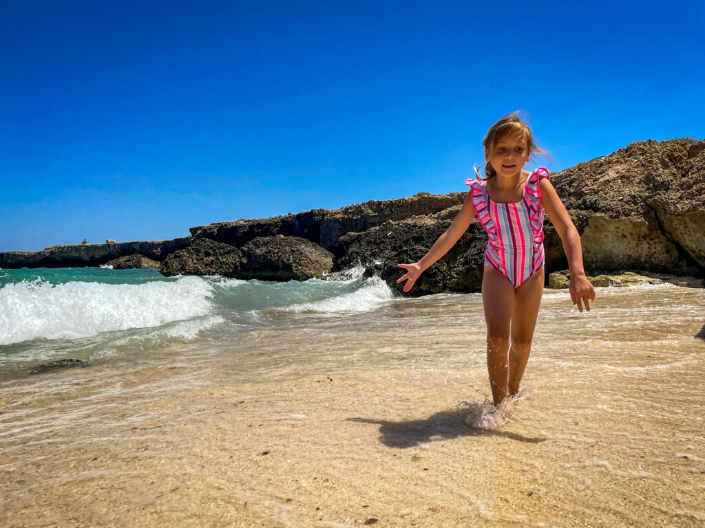 A young girl walks across the beach in Puglia, one of the best places in Europe to visit with outdoor kids.