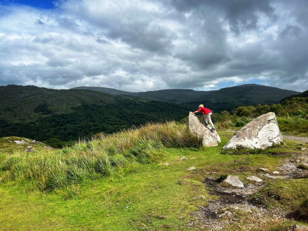A young boy climbs a rock at Killarney National Park in Ireland, one of the best places to visit in Europe with outdoor kids.