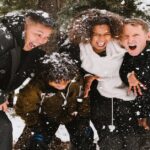 Four teens huddle together while playing in the snow, and wearing their warm winter layers!