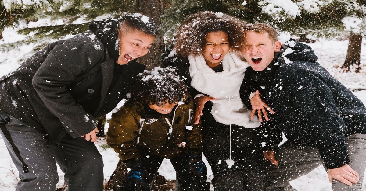 Four teens huddle together while playing in the snow, and wearing their warm winter layers!