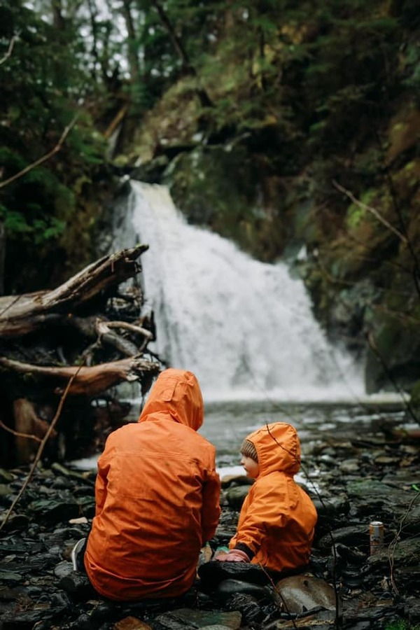 A mom and her young kids sit along a trail, taking a break from hiking in the rain.