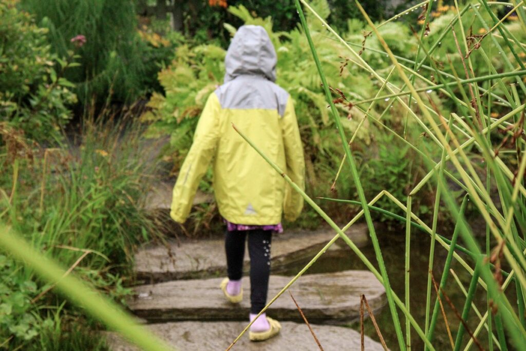 A young girl walks across a stone pathway, while hiking in the rain.