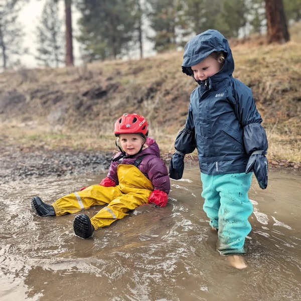 Two kids enjoy time in the mud while hiking in the rain.