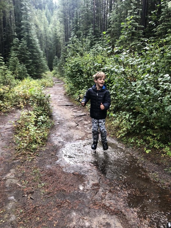 A young boy jumps in the mud while hiking in the rain.